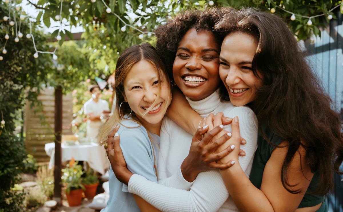 peachford-hero-mobile Three women smiling and hugging outdoors in a garden setting